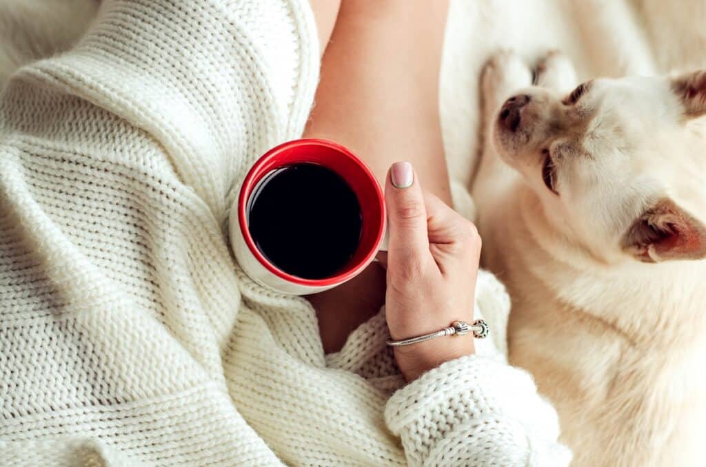 A woman have a lazy day drinking a cup of coffee and sitting with her dog.