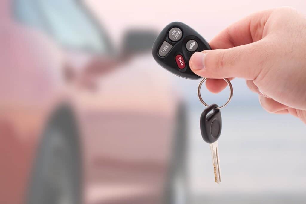 A hand holding car keys with a car in the background, illustrating potentially renting a car on Turo.