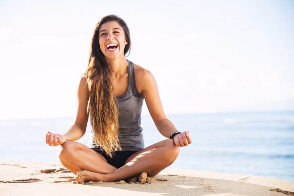 A happy young woman meditating and laughing about money by the beach.