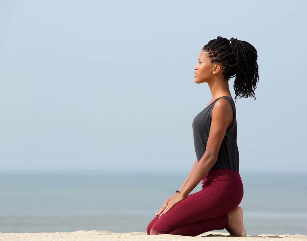A woman meditating at the beach thinking about money manifestation.