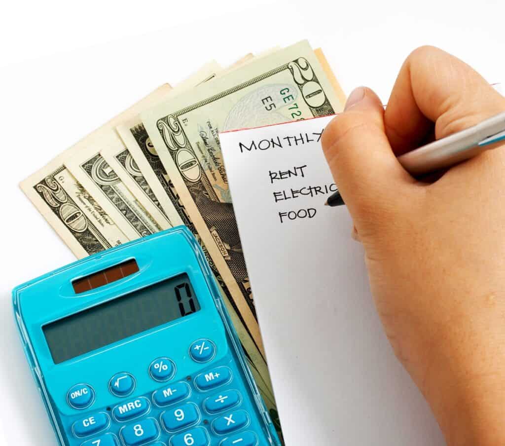 A person writing a list of expenses with a calculator next to them.