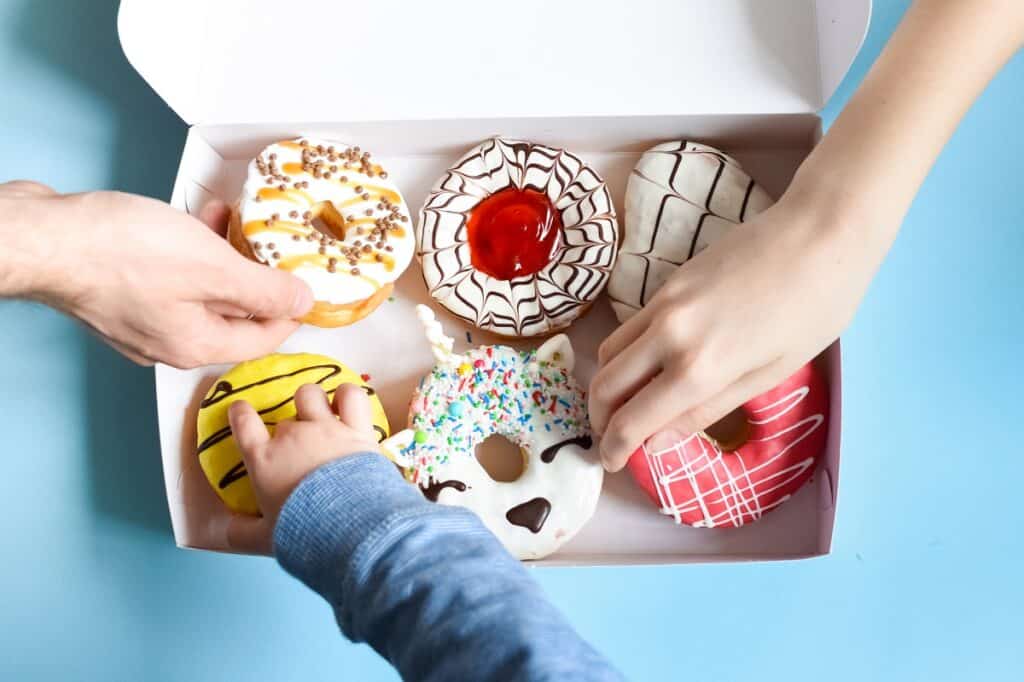 Hands reaching for donuts in a donut box.