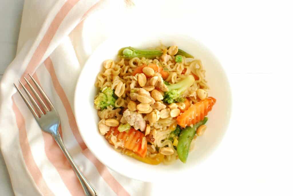 A bowl of ramen veggie stir fry topped with peanuts.