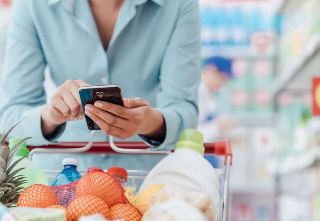 A woman grocery shopping and looking at her phone.