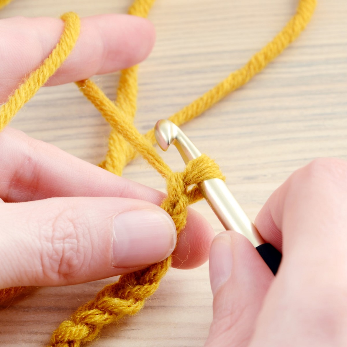 A woman's hands crocheting with yellow yarn.