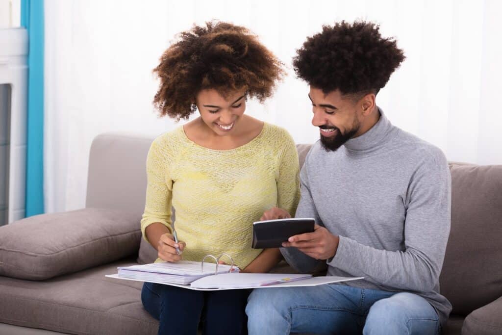 A happy couple sitting on the couch with a calculator and paper working on their budget.