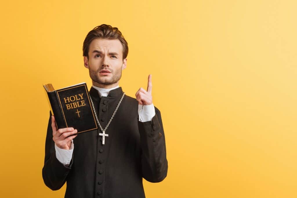 A pastor holding a bible and pointing his finger in the air, like he just thought of an idea.