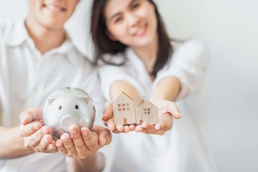 A couple holding a piggy bank and a mini house to represent saving for their joint goals.