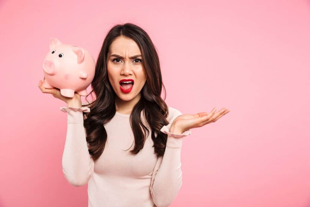 A woman upset about not having money saved, holding a piggy bank.