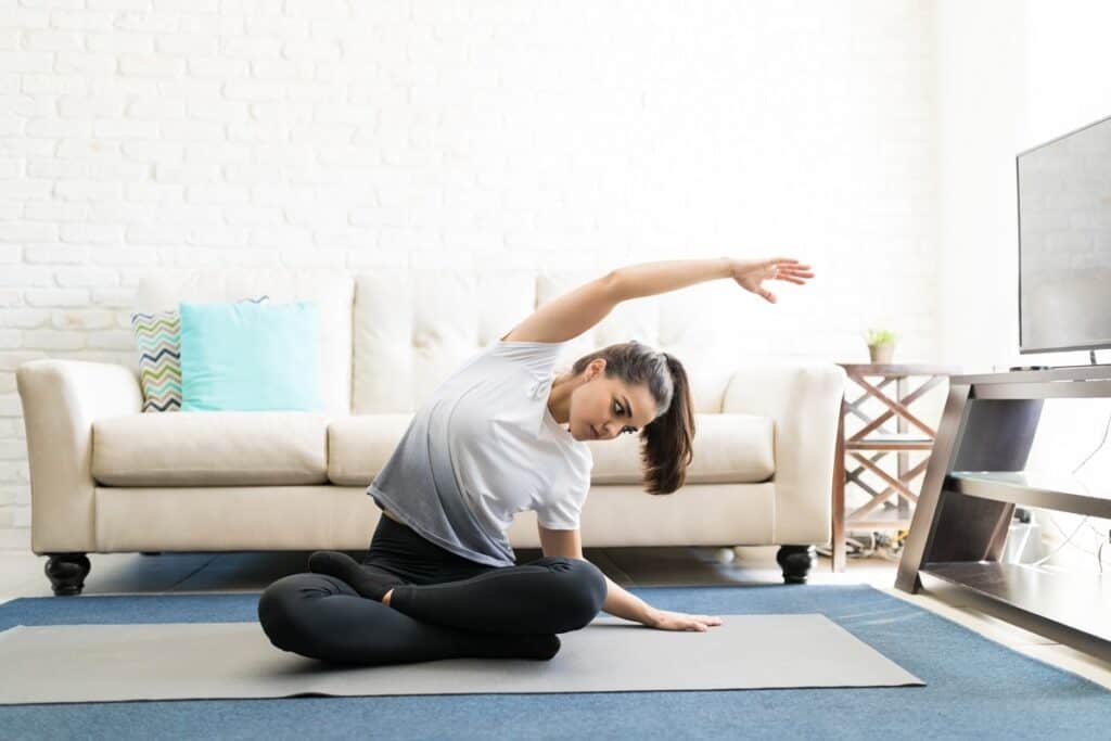A woman doing yoga on a mat in her living room as a form of cheap self care.