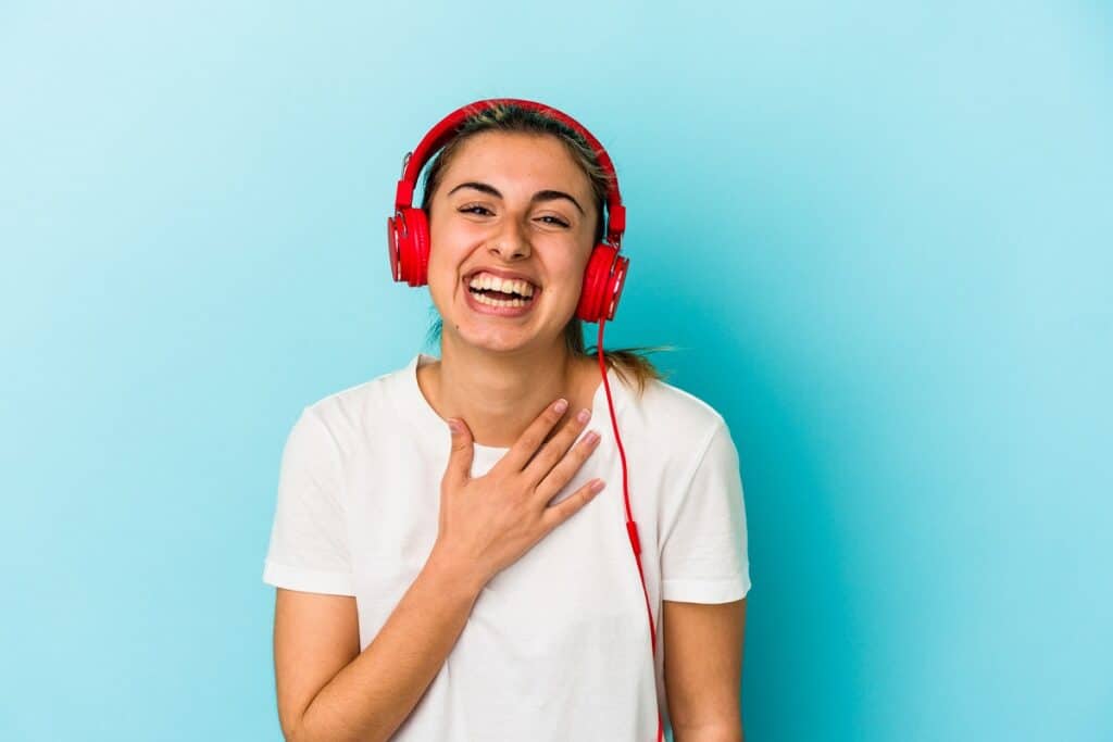 A woman laughing listening to stand up comedy via headphones for self care.