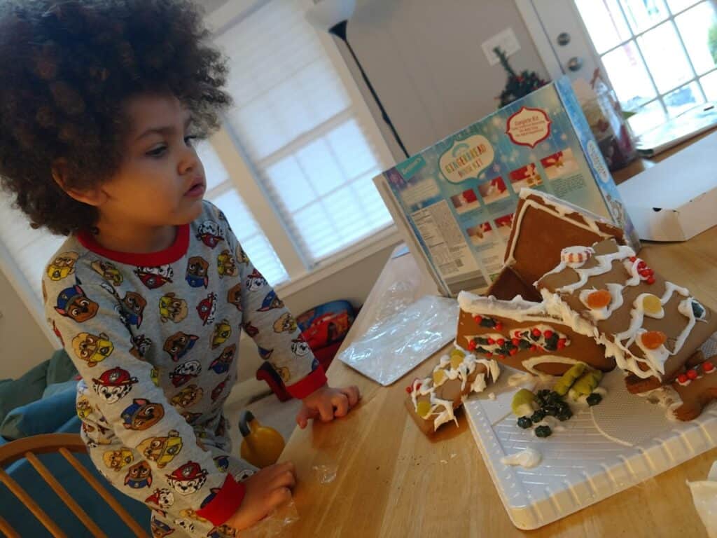 A little kid building a gingerbread house.